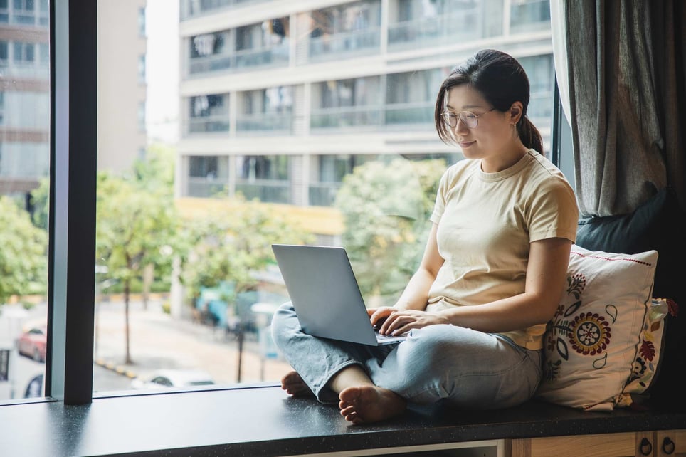 Asian-woman-sitting-by-the-window-using-laptop-how-to-decide-between-current-job-and-new-job