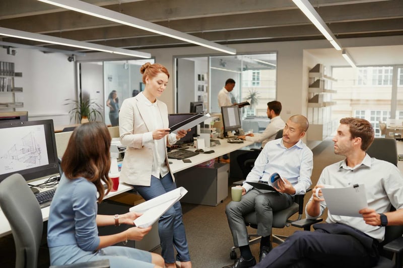 Business-Team-Looking-At-Boss-Leaning-Against-Desk-how-to-give-feedback-to-your-boss