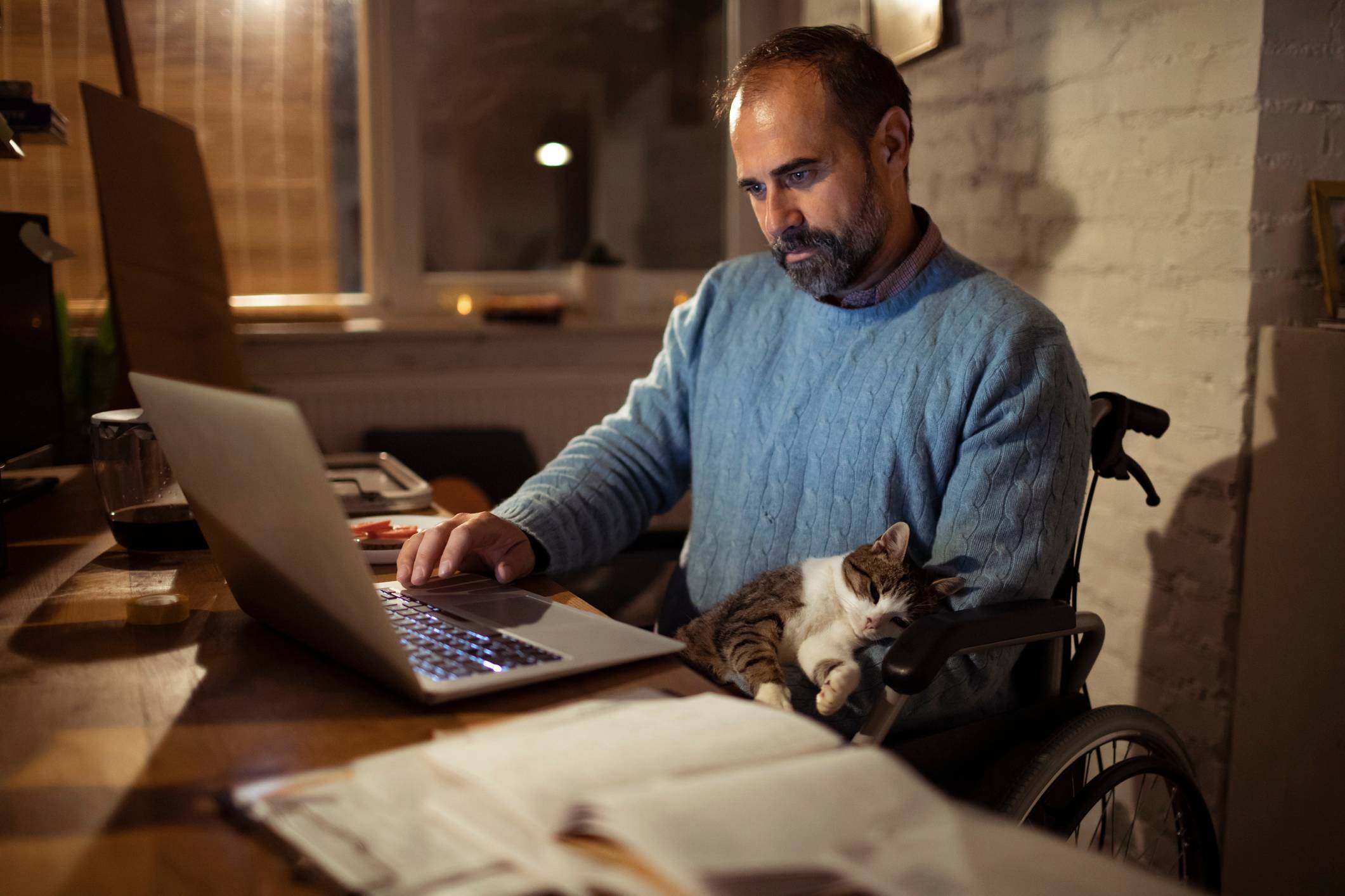 Close-up-of-a-man-sitting-in-a-wheelchair-at-home-with-his-cat-working-on-the-laptop-purpose-of-fear