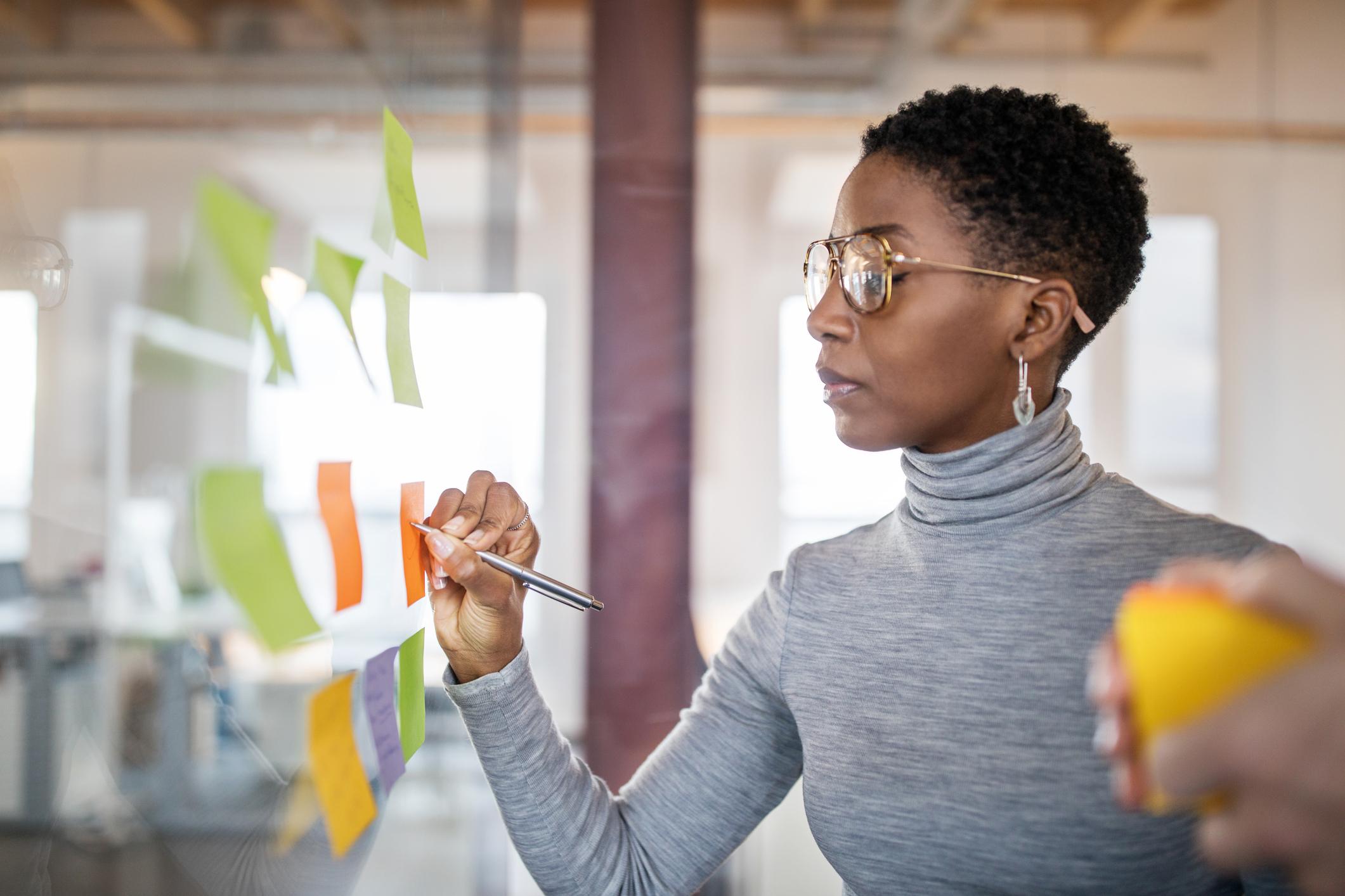 Confident-mid-adult-businesswoman-writing-new-ideas-onto-a-adhesive-note-career-statement