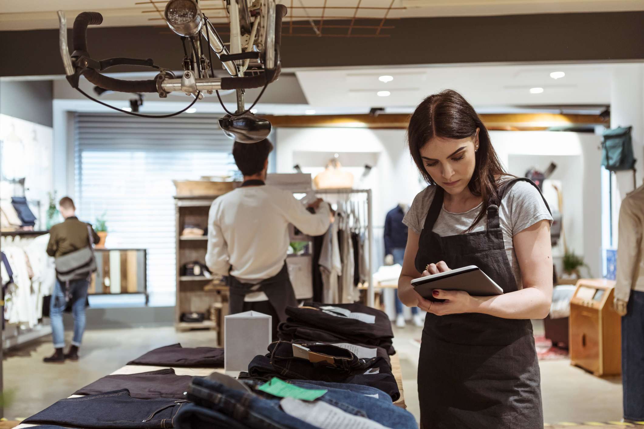 Female-owner-using-digital-tablet-while-coworker-arranging-clothes-on-rack-at-store-what-is-commission-pay