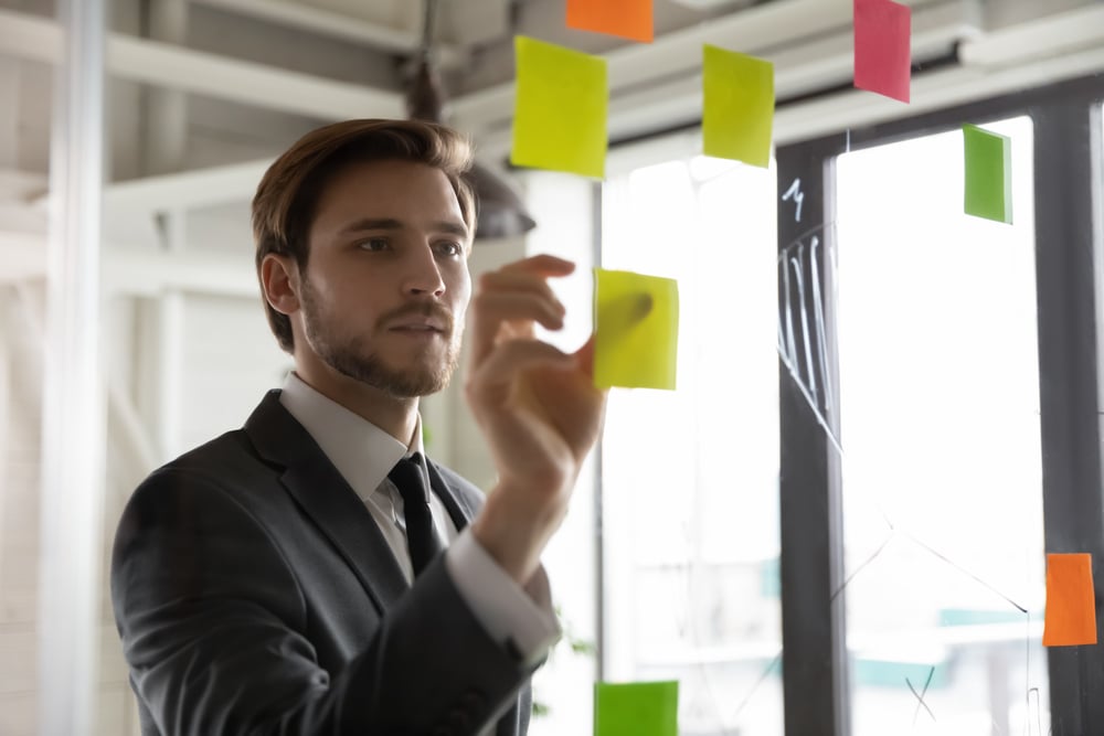 Focused-young-male-employee-write-ideas-on-sticky-notes-hard-work-vs-smart-work