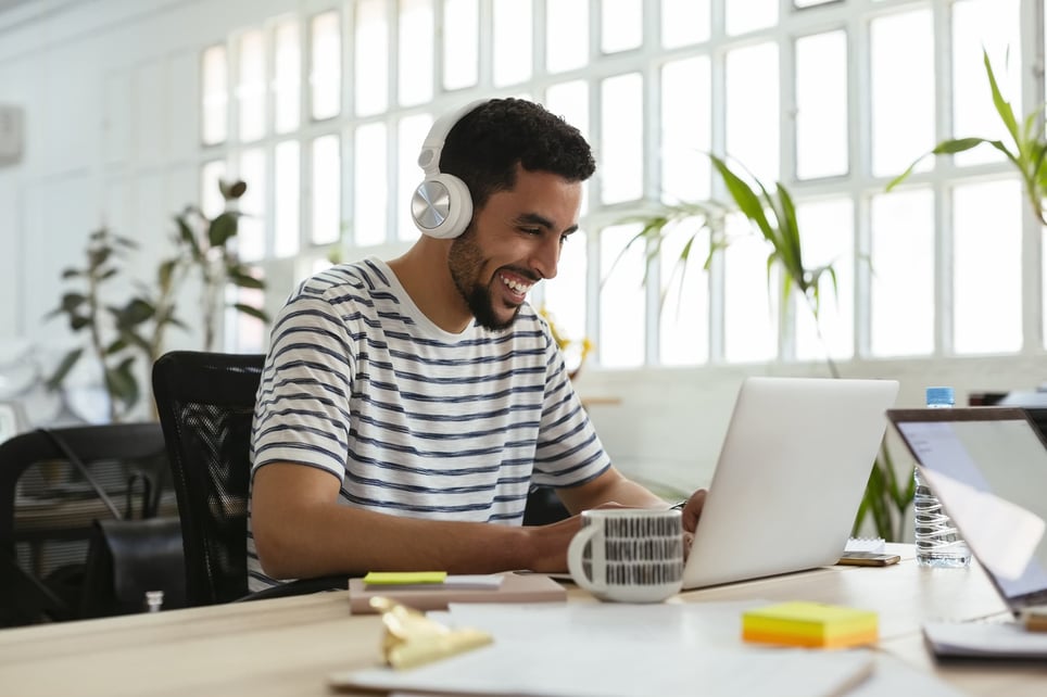 Laughing-young-man-wearing-headphones-using-laptop-at-desk-in-office-ice-breakers-for-virtual-meetings