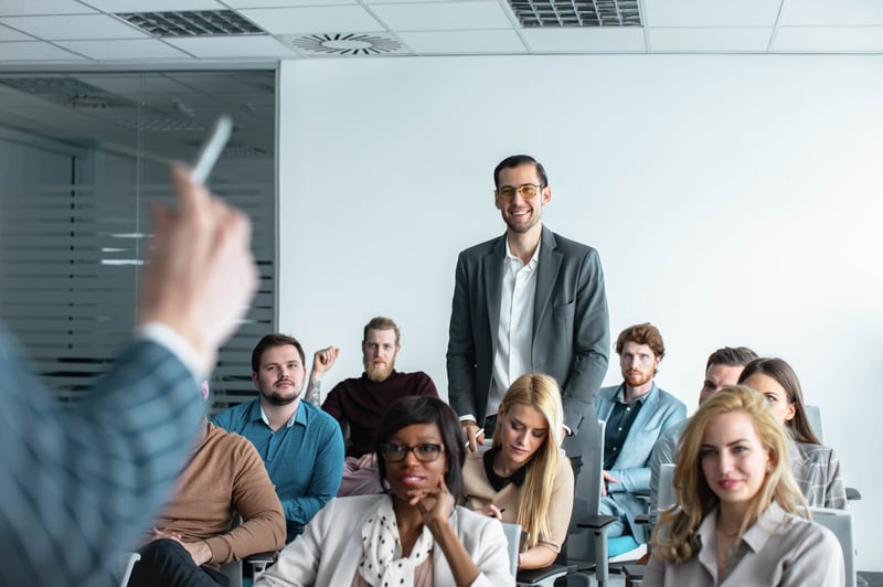 Man-Standing-Amongst-Businesspeople-During-Corporate-Training-overqualified-for-job