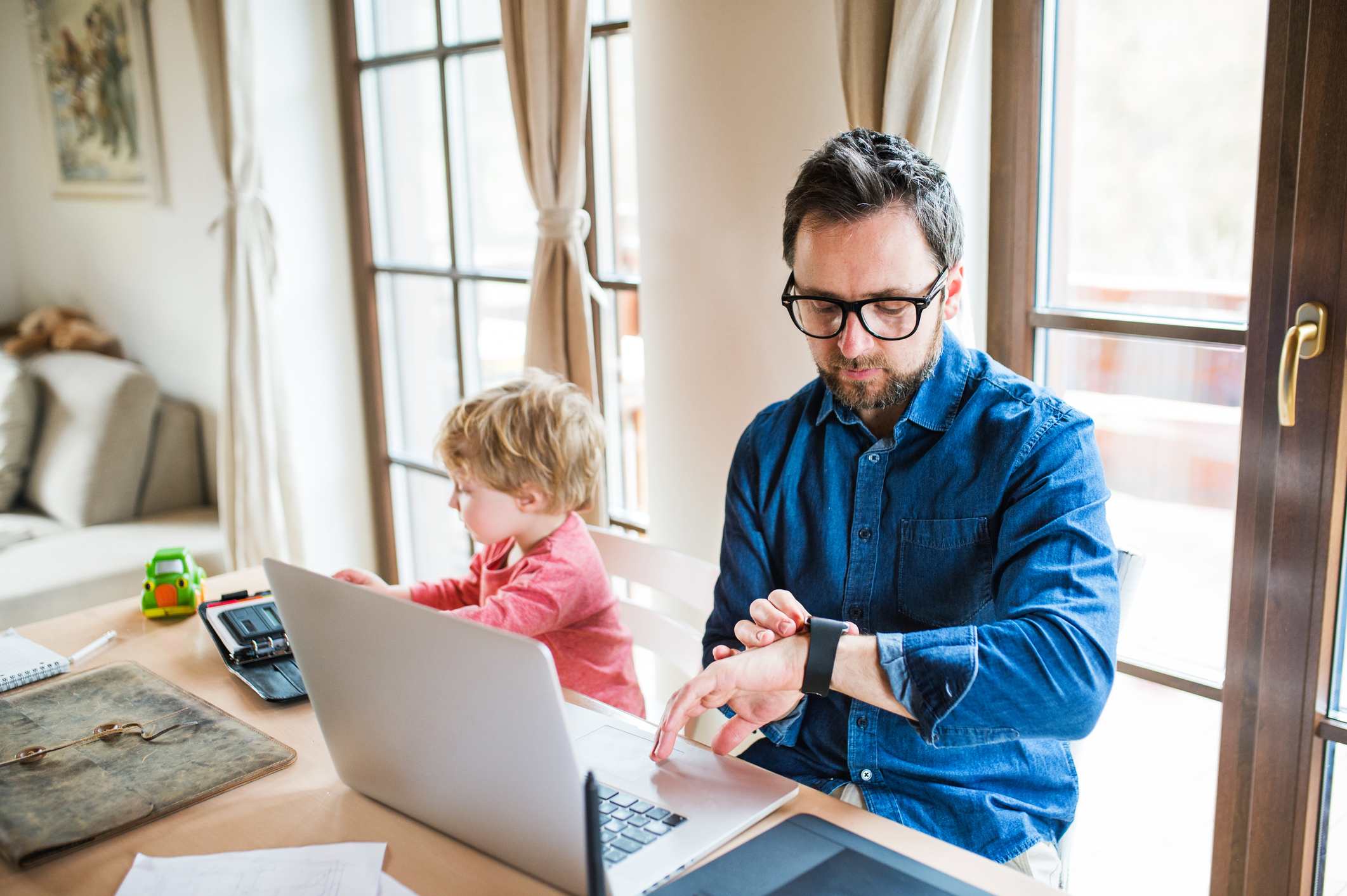 Man-at-home-with-his-son-while-working-from-laptop-and-looking-at-watch-is-hourly-or-salary-better