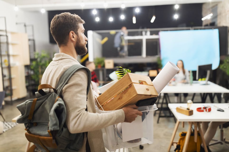 Man-holding-box-of-belongings-after-being-let-go-laid-off-vs-fired