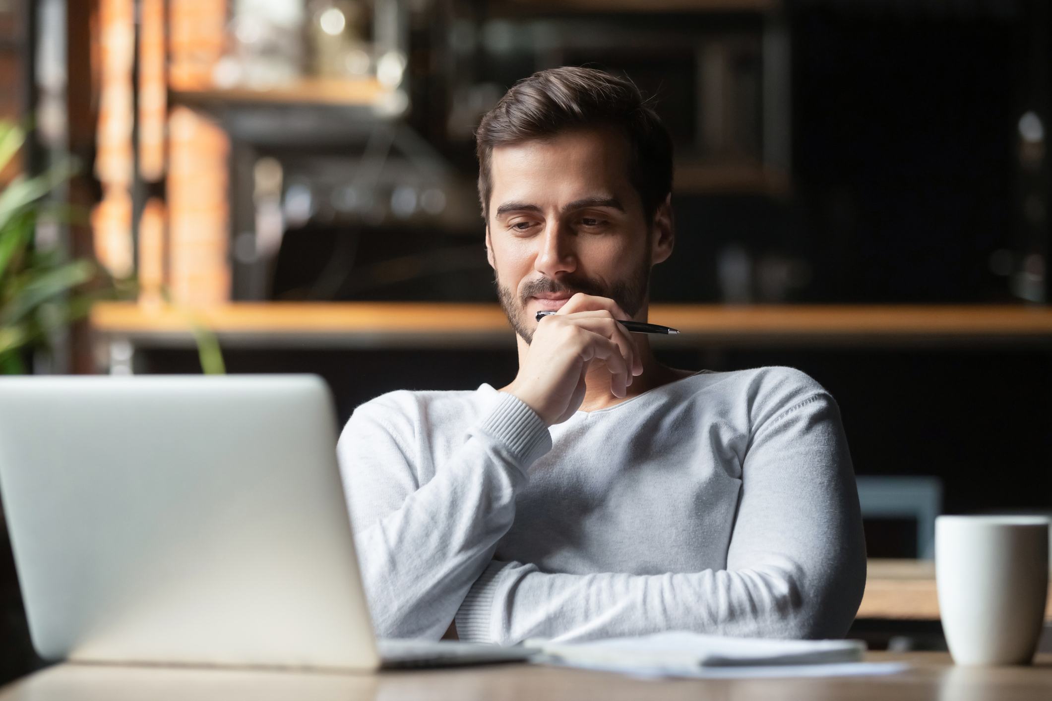 Man-holding-pen-thinking-and-looking-at-laptop-how-to-respond-to-a-job-rejection-email