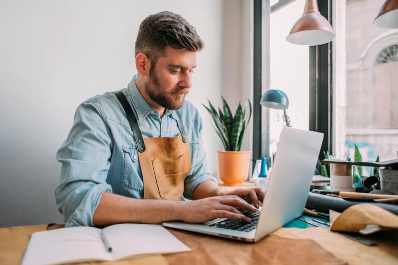 Man-sitting-in-his-workshop-writing-an-email-on-laptop-thank-you-to-a-team