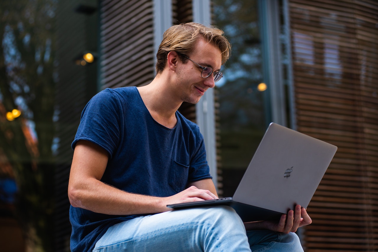 Man-using-his-laptop-sitting-in-stairs-at-college-magna-cum-laude-vs-summa-cum-laude