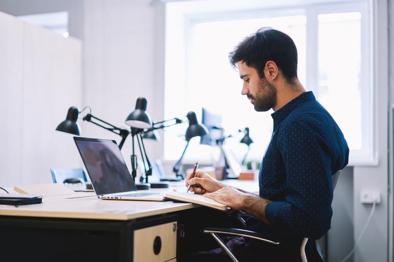 Man-writing-on-notebook-at-his-desk-first-day-on-the-job