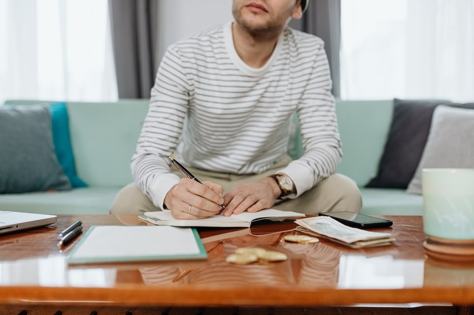 Man-writing-on-notebook-while-counting-money-how-to-budget