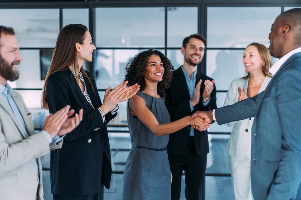 Manager-shaking-new-hires-hand-in-front-of-team-email-before-first-day-of-work