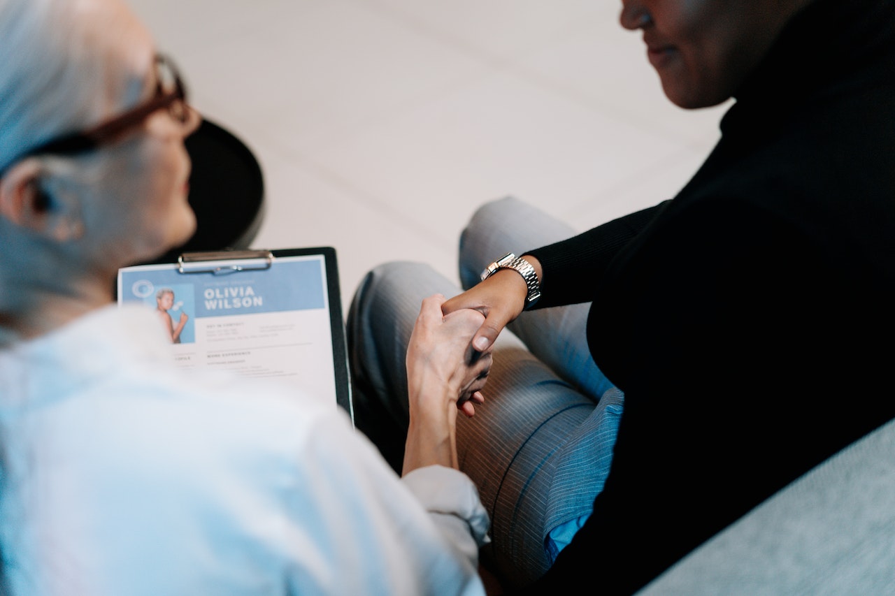 Older-woman-shaking-hand-of-man-after-interview-with-resume-on-her-hand-how-to-put-babysitter-on-a-resume