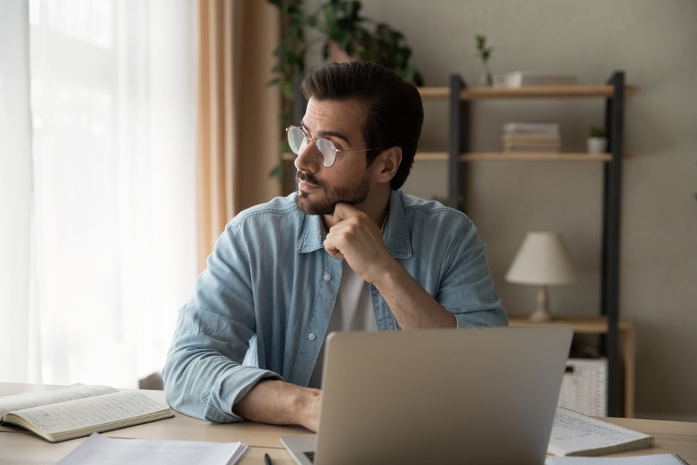 Pensive-young-guy-employee-sit-at-workplace-overemployed