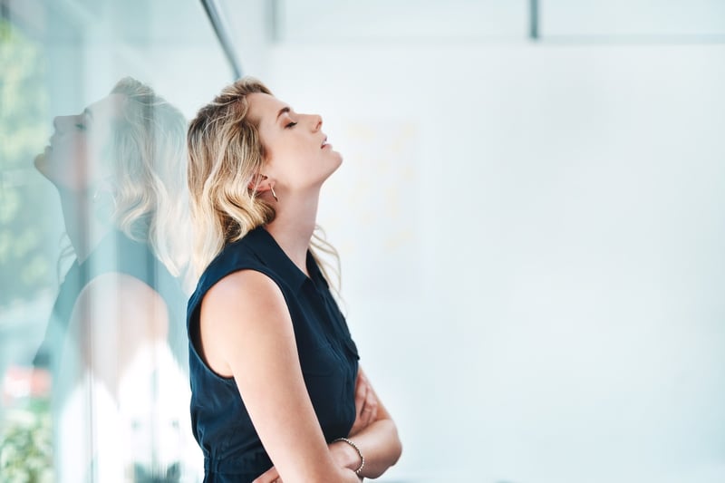 Sad-business-woman-with-eyes-closed-leaning-against-window-at-work-crying-at-work