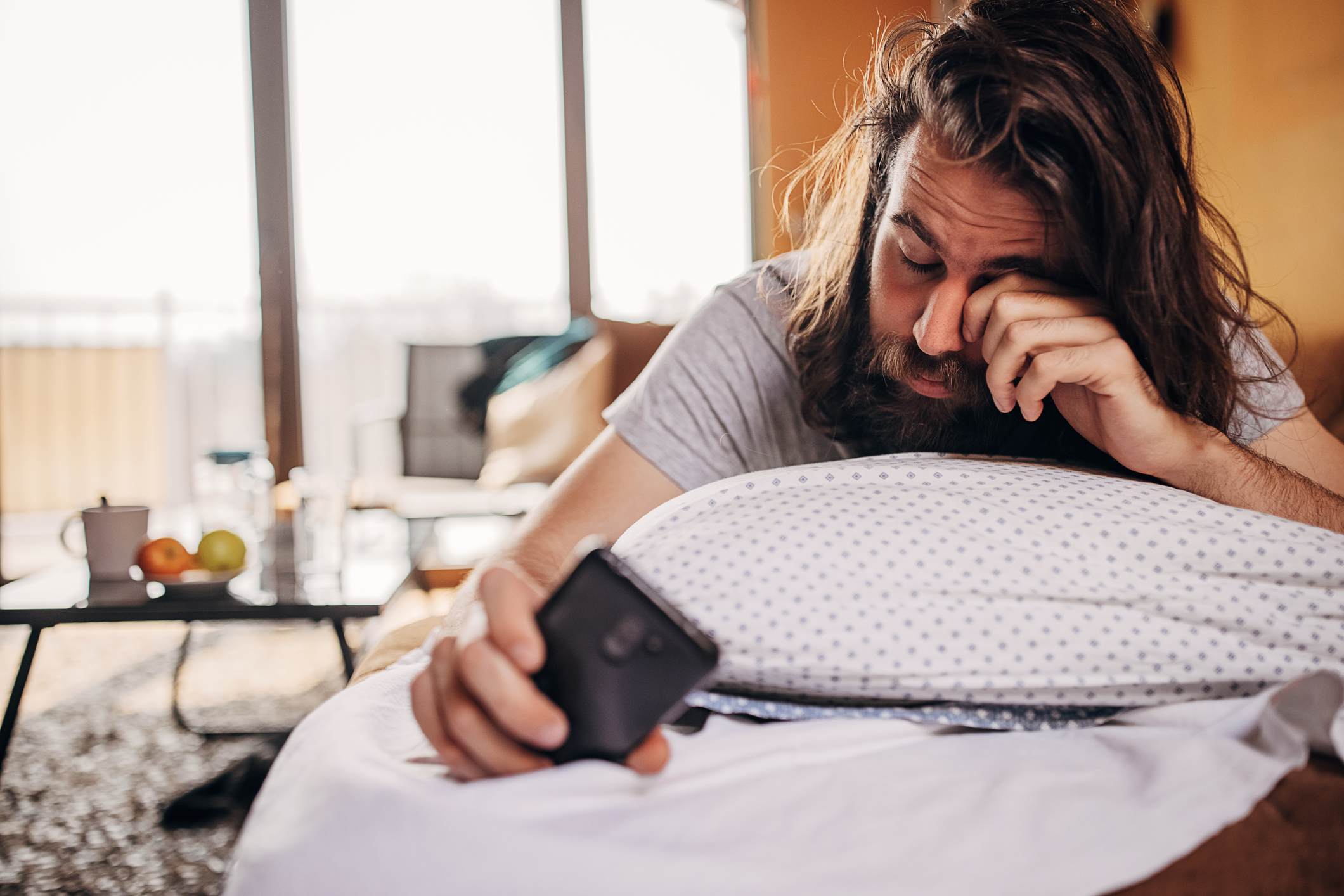 Sleepy-man-at-home-setting-alarm-on-phone-at-the-middle-of-the-day-how-to-adjust-to-night-shifts