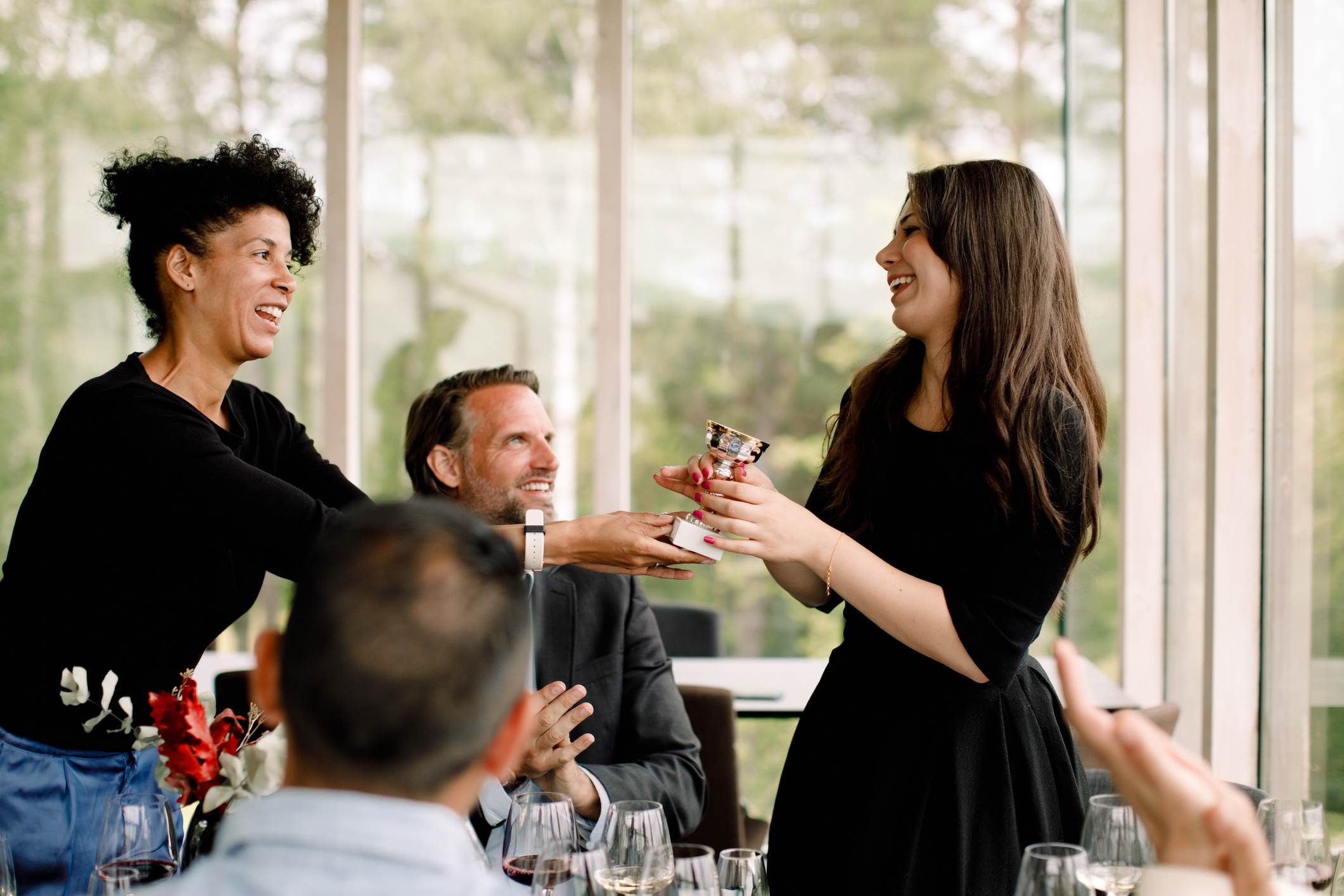 Smiling-businesswoman-giving-trophy-to-female-colleague-appreciate-a-team