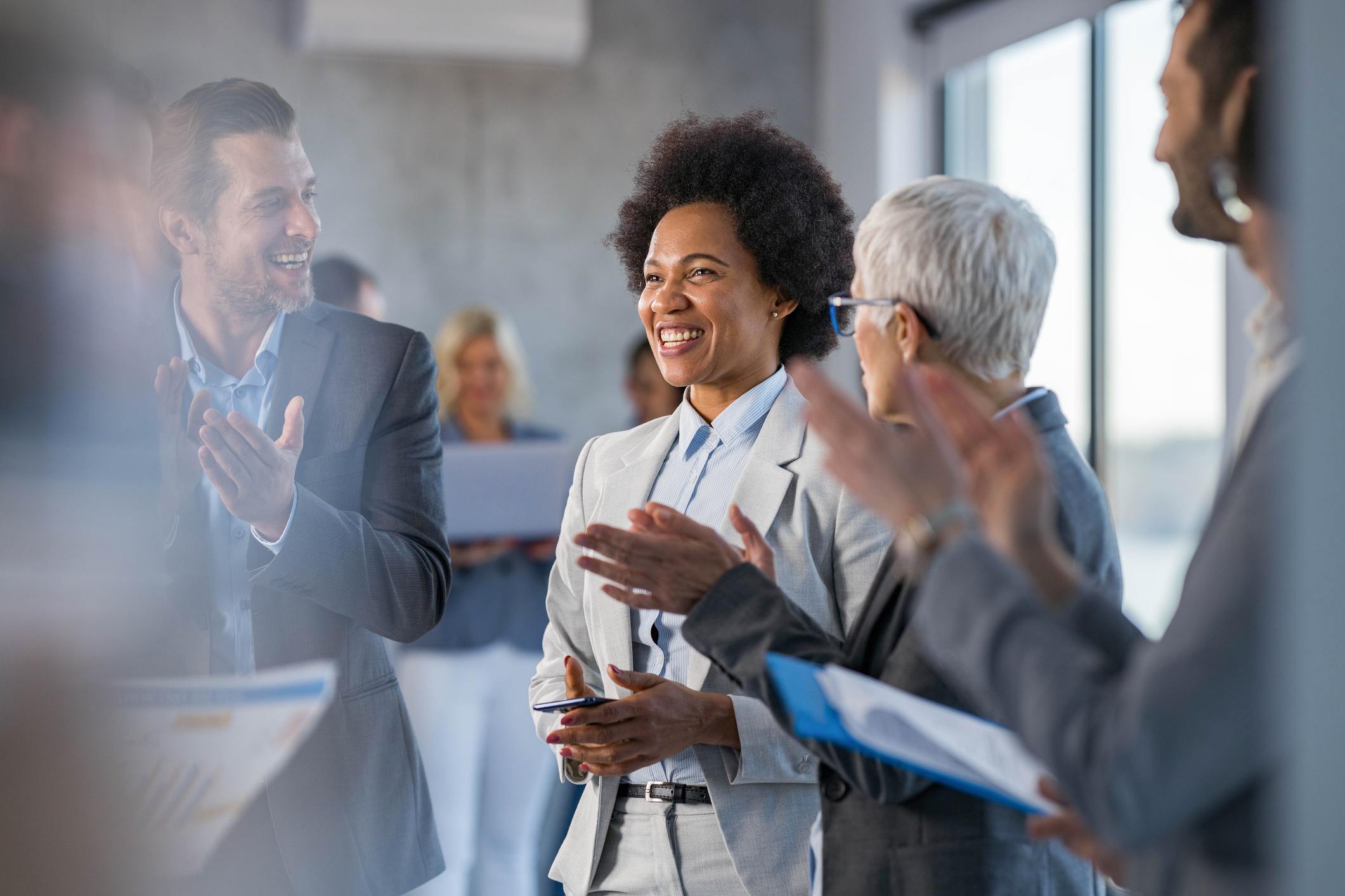 Team-congratulating-smiling-coworker-at-office-breaking-down-silos