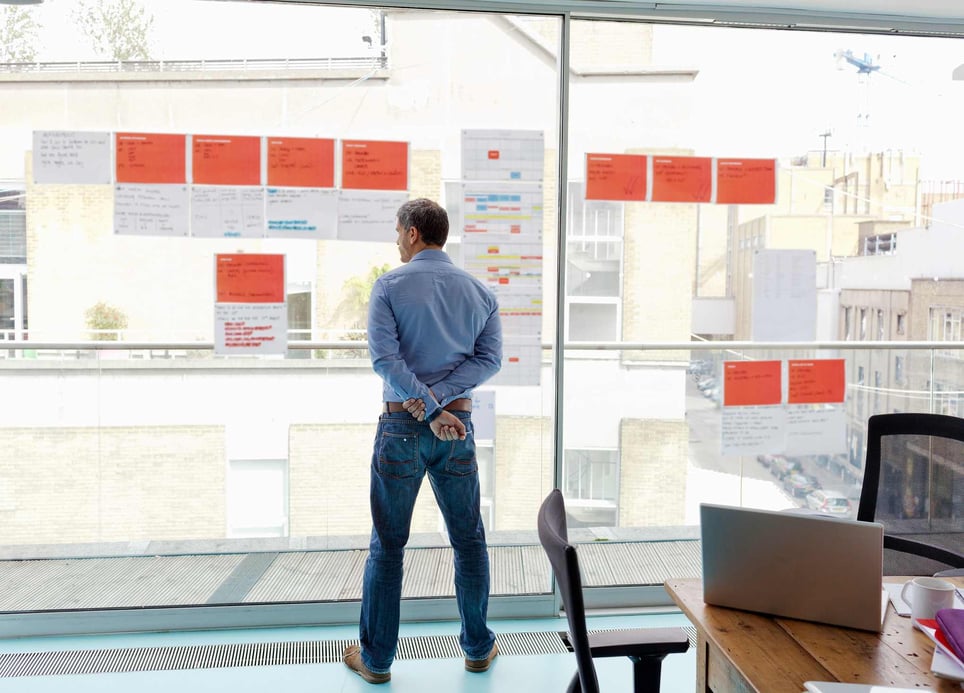 Thoughtful-man-standing-in-front-of-office-window-taking-a-sabbatical-from-work