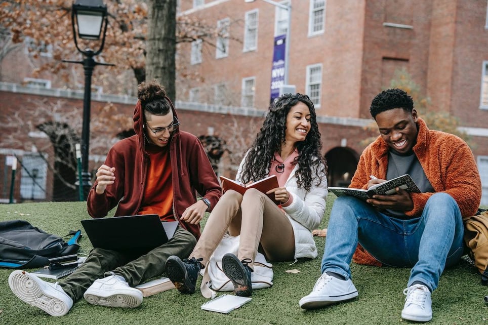 Three-friends-sitting-on-college-campus-laughing-and-studying-interpersonal-relationships