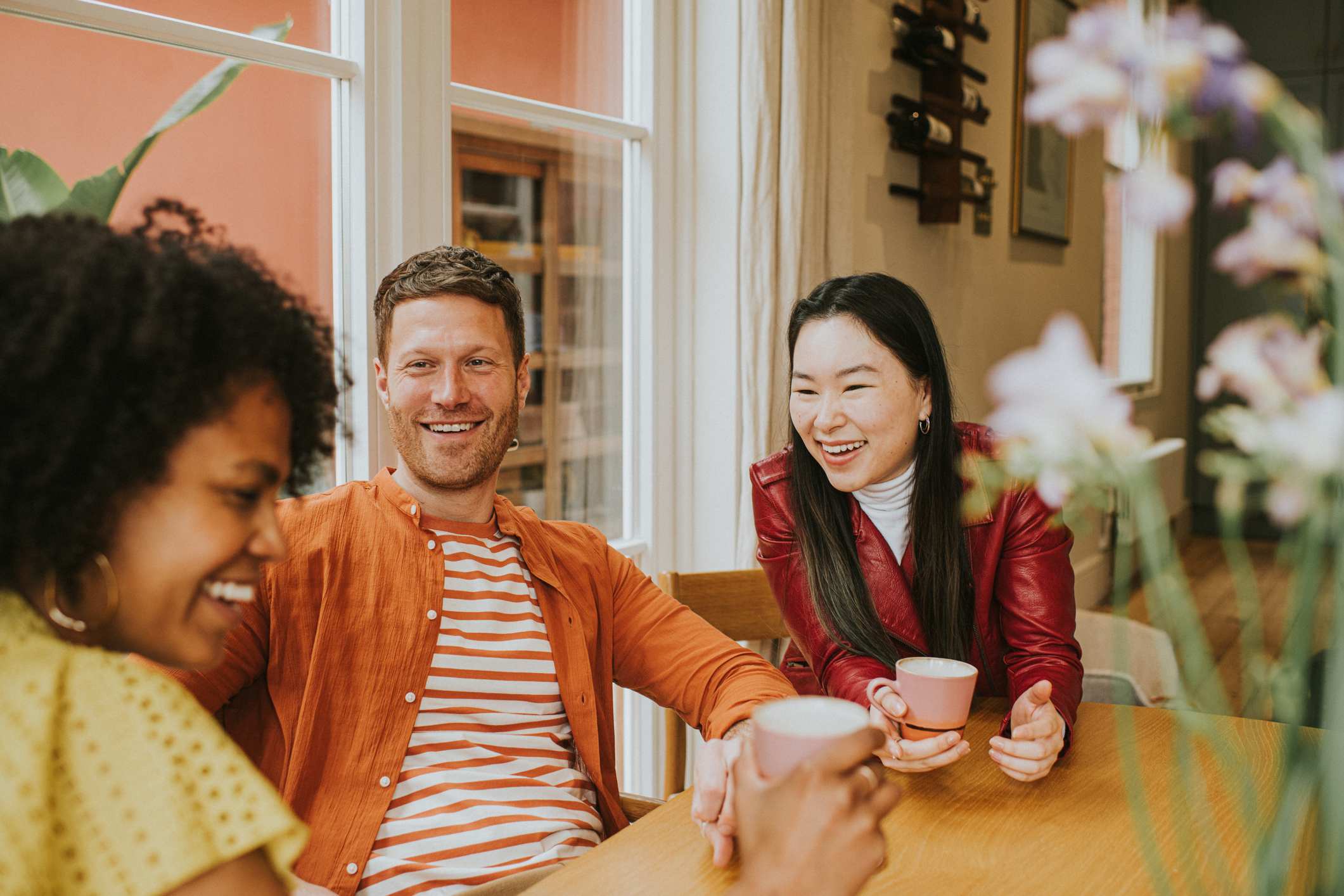 Three-young-people-sit-around-a-table-and-giggle-as-they-have-a-lighthearted-discussion-and-drink-coffee-how-to-make-life-meaningful