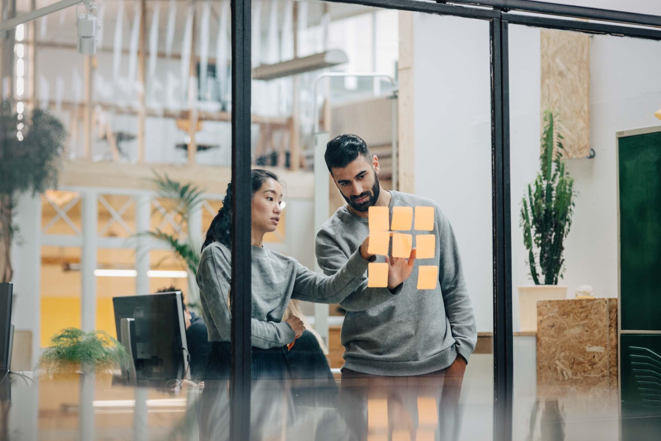 Two-concentrated-coworkers-looking-at-post-its-working-together-breaking-down-silos