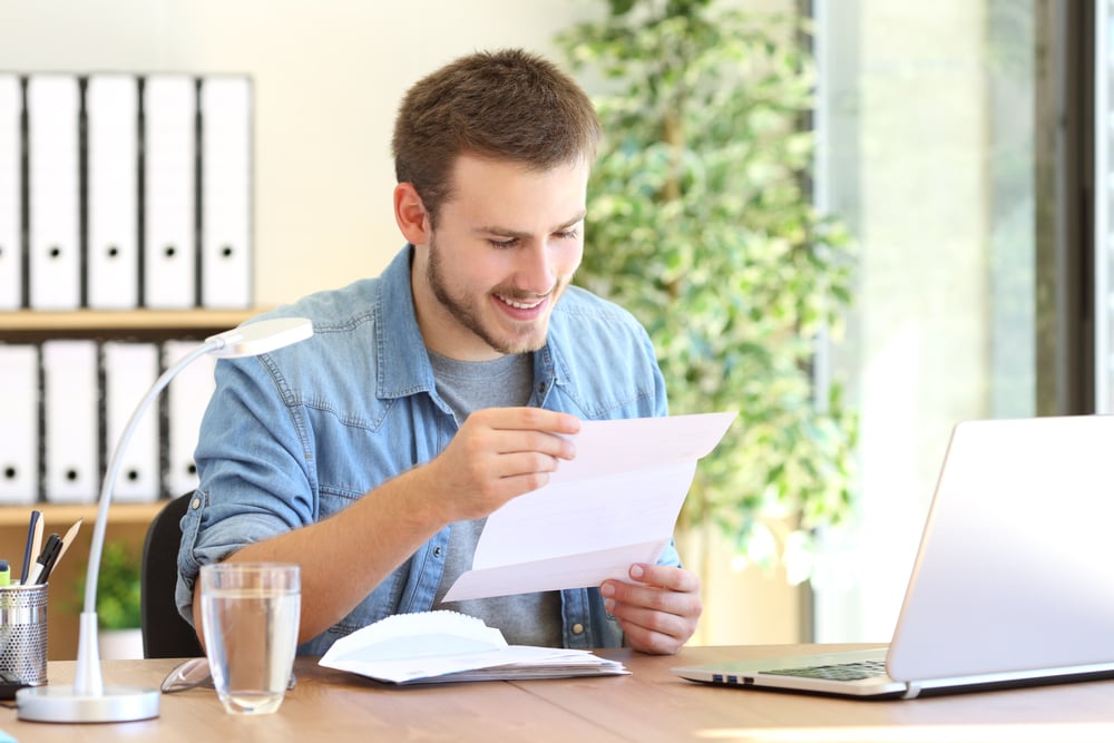 White-man-reading-a-letter-in-front-of-laptop-holiday-messages-to-employees