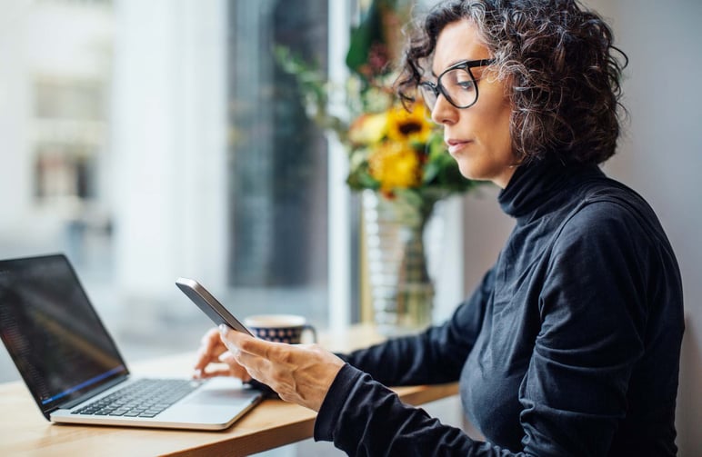 Woman-procrastinating-on-phone-in-front-of-laptop-what-causes-procrastination