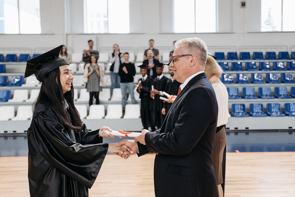 Woman-recieving-diploma-from-college-dean-at-graduation-ceremony-magna-cum-laude-vs-summa-cum-laude