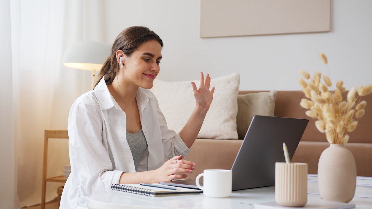 Woman-saying-hi-with-her-hand-at-virtual-interview-with-tablet-virtual-interview