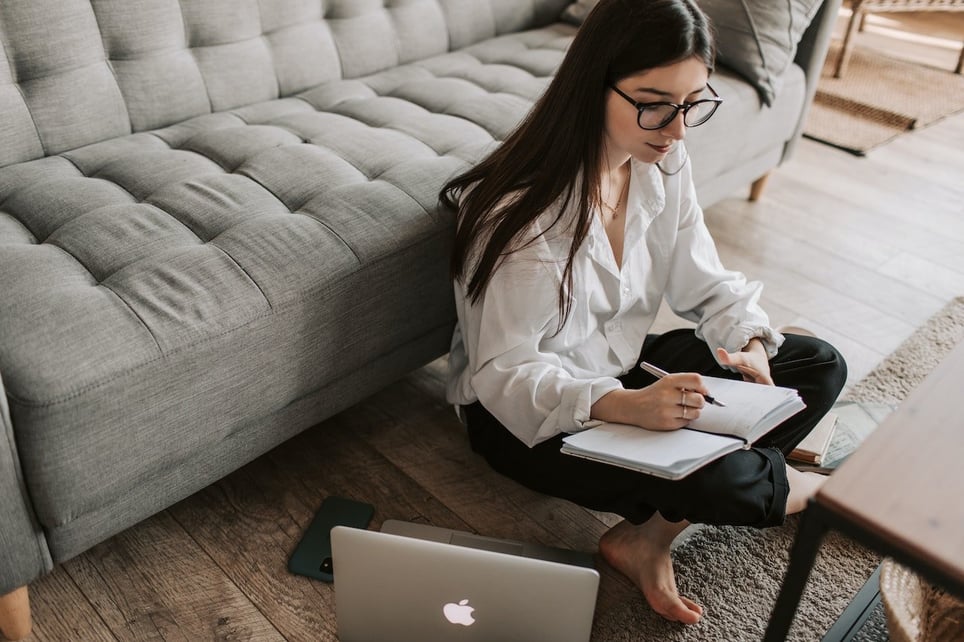 Woman-sitting-on-her-living-room-floor-with-laptop-and-writing-on-notebook-character-references