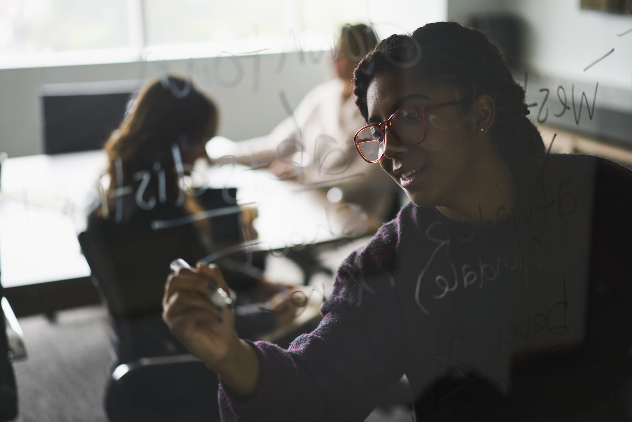 Woman-writing-on-glass-wall-in-conference-room-monthly-goals-examples