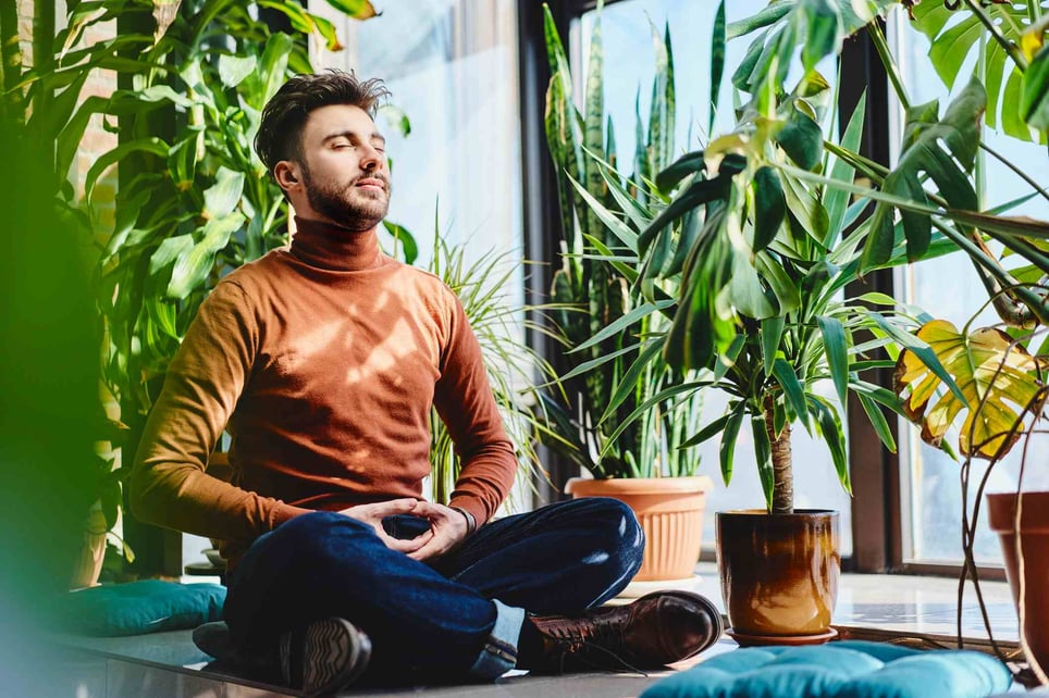 Young-man-meditating-by-plants-on-window-sill-at-home-anger-management-strategies