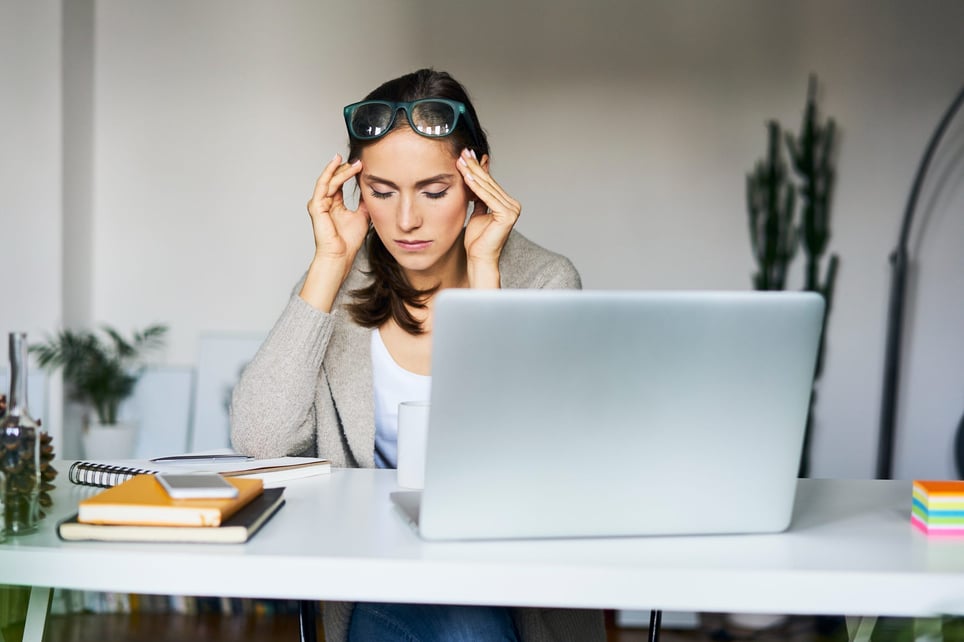 Young-woman-at-home-with-laptop-on-desk-touching-her-temples-causes-of-workplace-stress