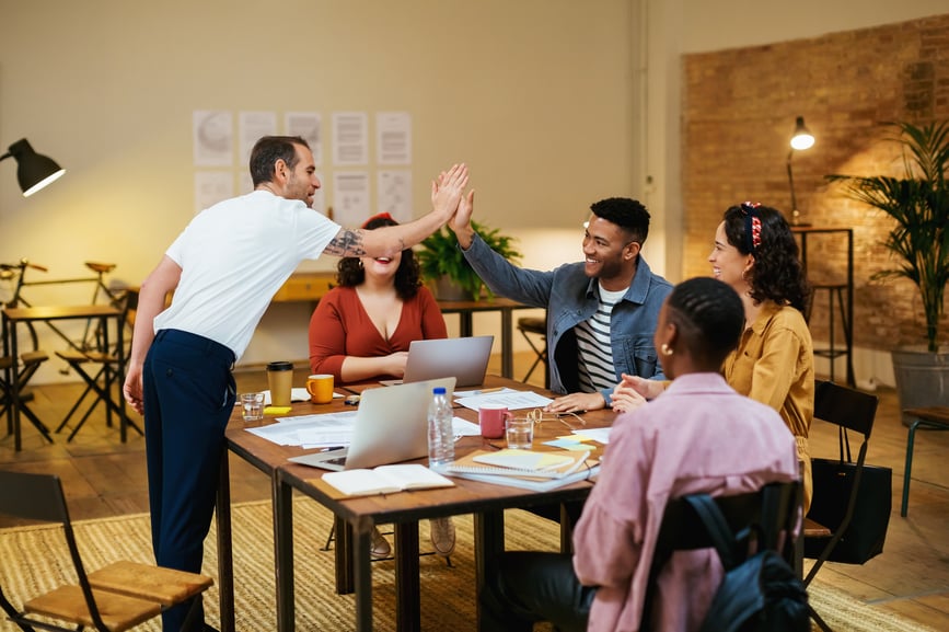 colleagues-sitting-around-a-table-and-the-other-two-high-five-work-motivation