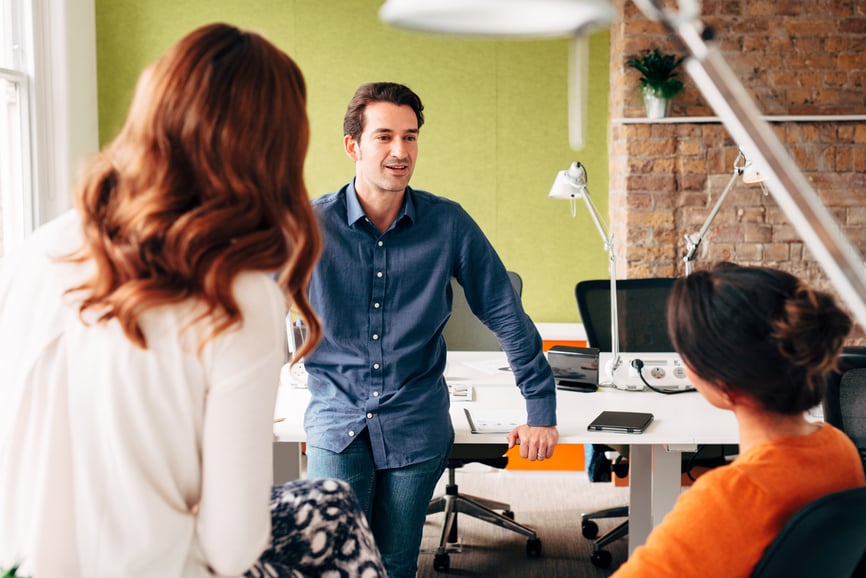 man-leaning-on-table-talking-to-colleagues-empowerment-at-work