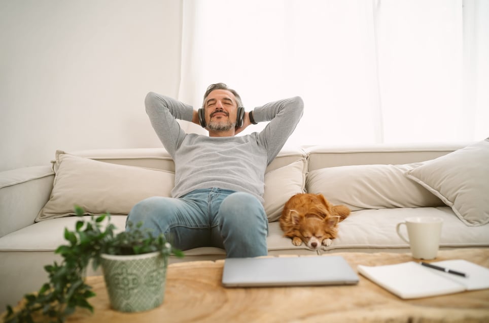 man-sitting-on-sofa-listening-to-music-with-dog-reasons-to-take-a-vacation