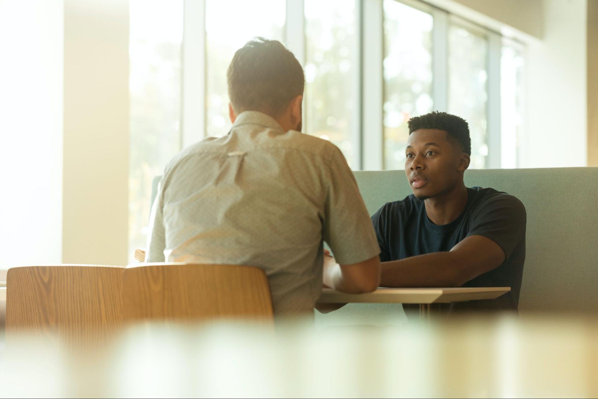 two-mean-sit-at-table-having-a-conversation-stress-management-techniques