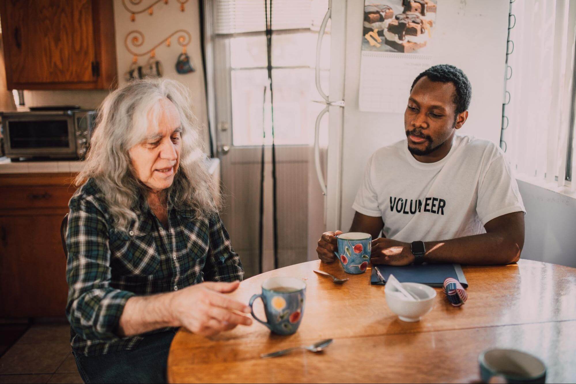 volunteer-sitting-at-table-with-elderly-lady-what-is-altruism